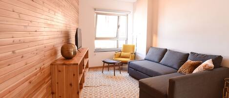 Una sala de estar moderna con una pared de madera, un sofá gris, un sillón amarillo y una alfombra estampada.