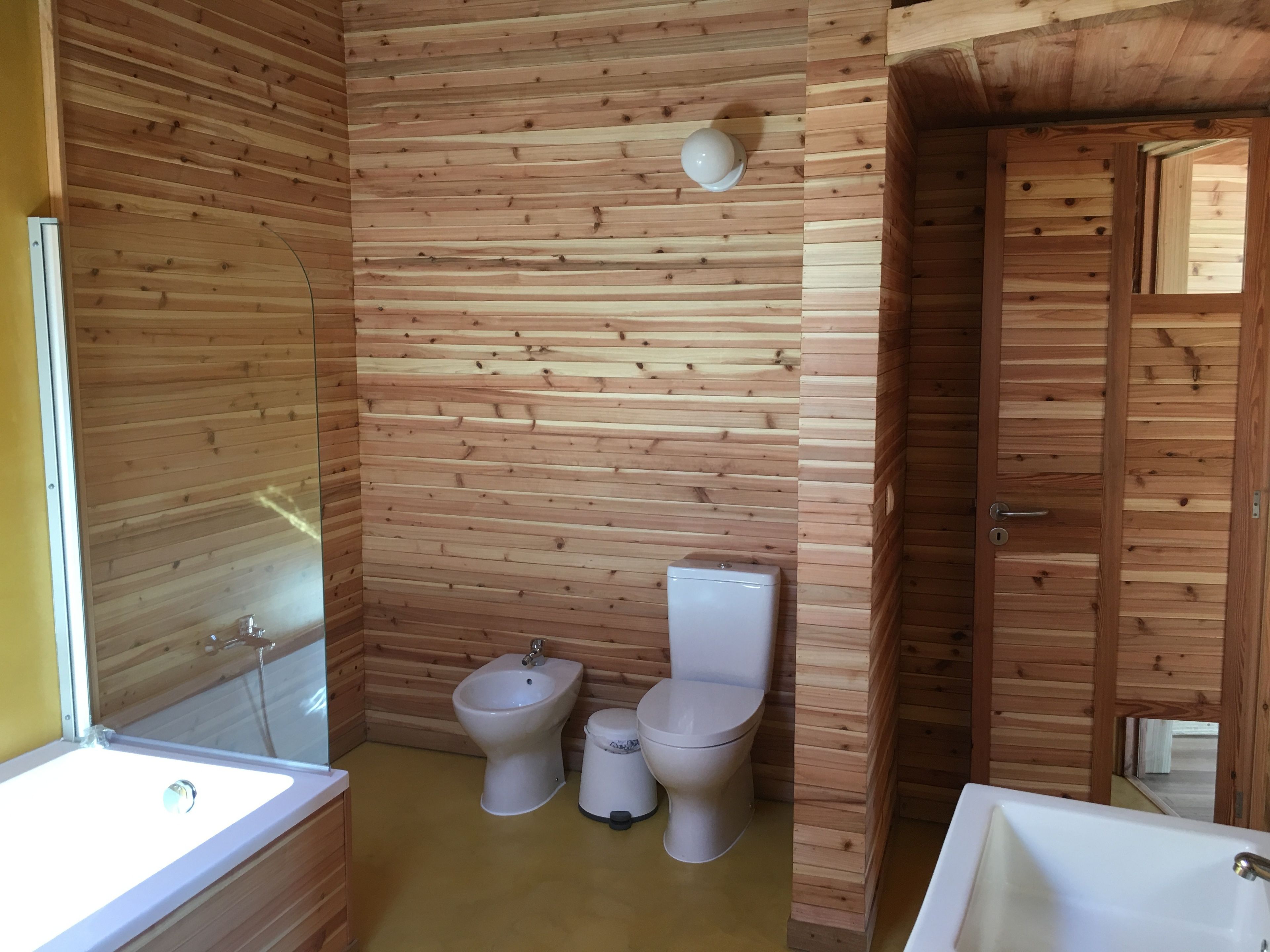 Een betegelde badkamer met een bad, een toilet en een hygiëneschuimer.