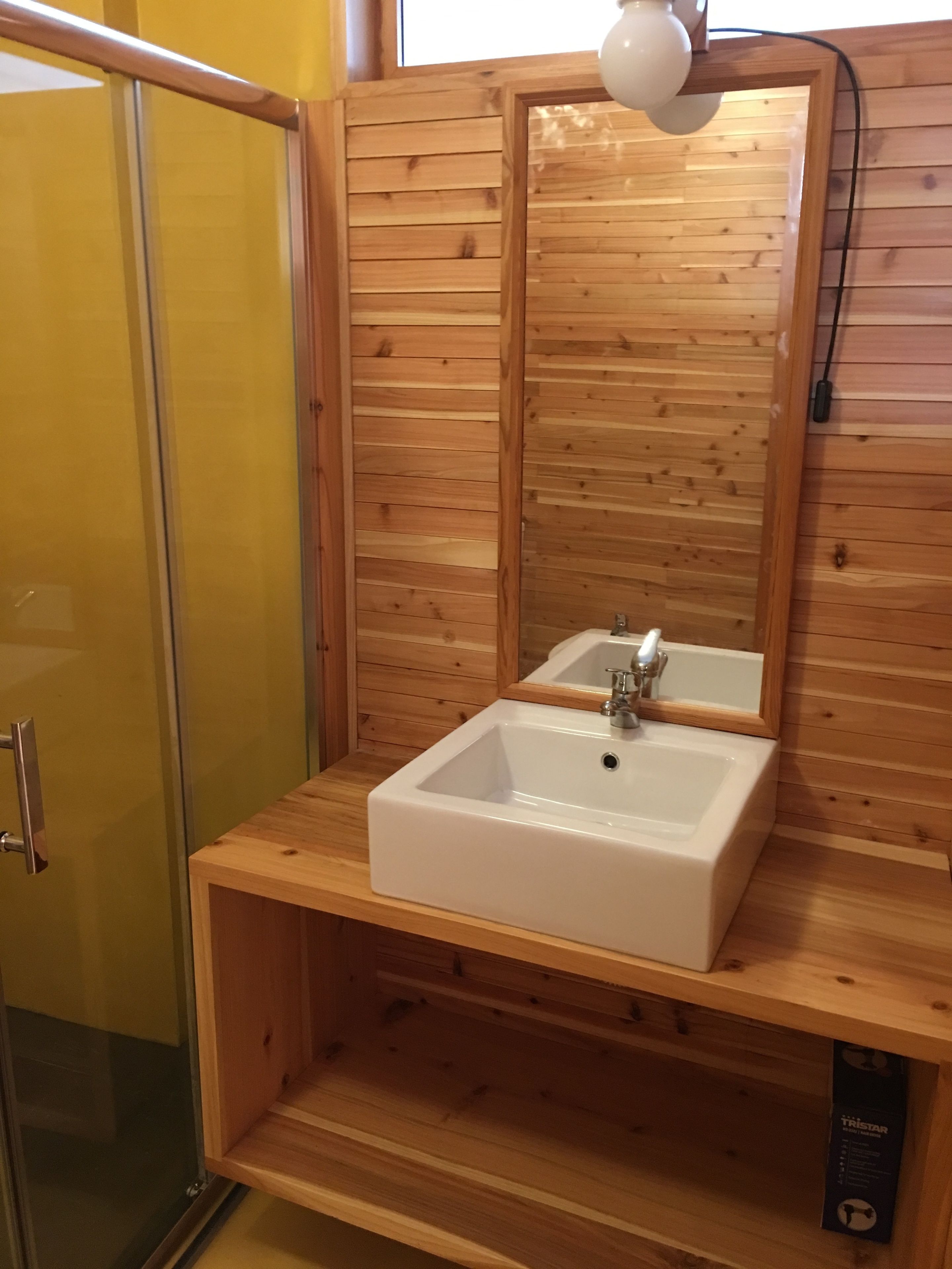 Un baño de madera con un lavamanos blanco, un espejo y una zona de ducha.