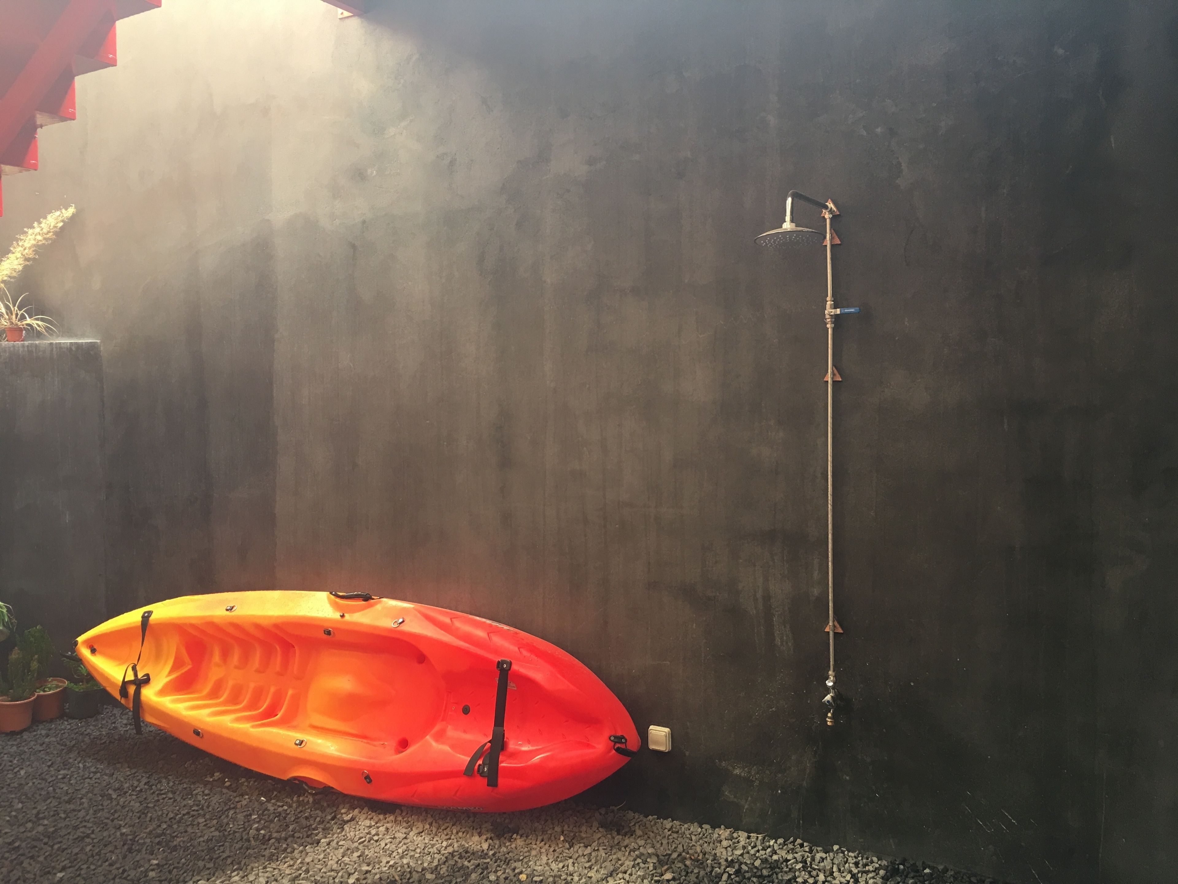 A red kayak next to a shower area with a vertical water spout.