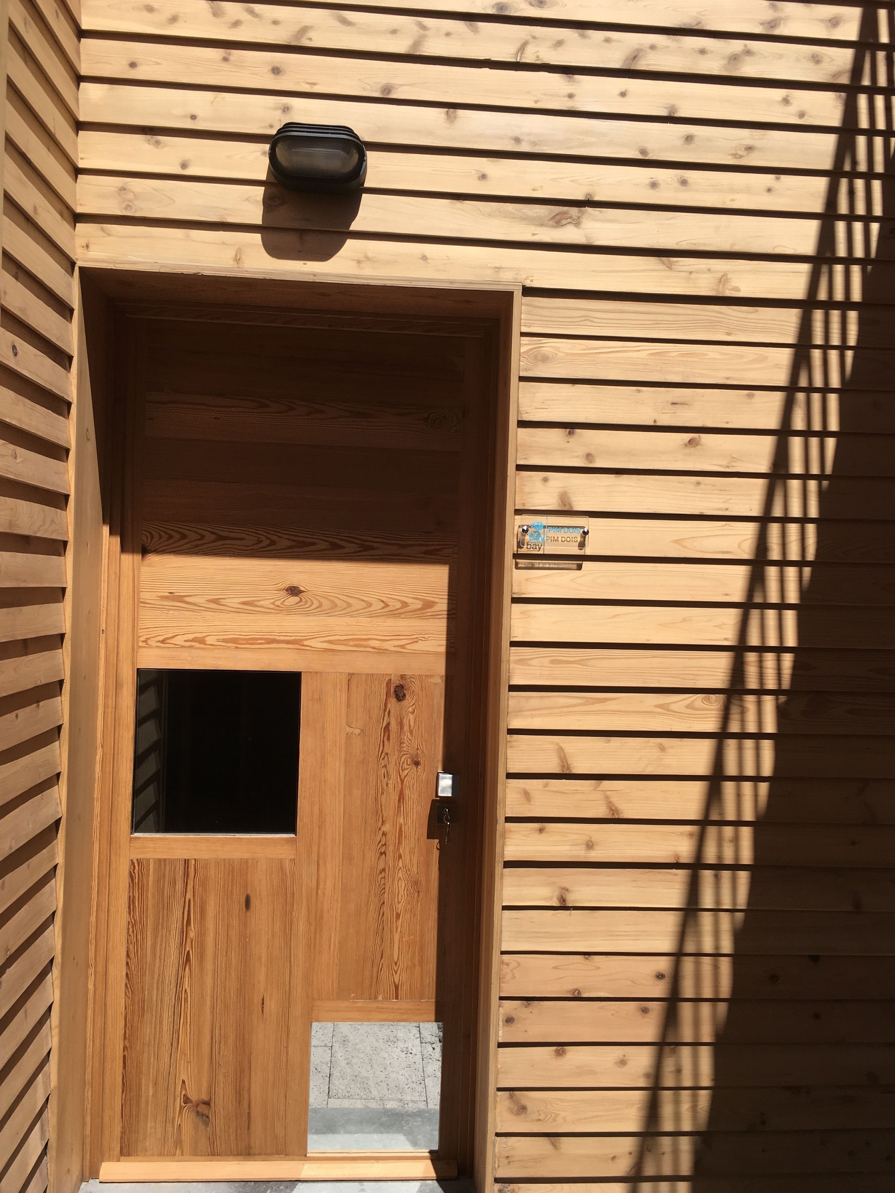 Une porte en bois avec une petite fenêtre et une boîte aux lettres fixée au mur.