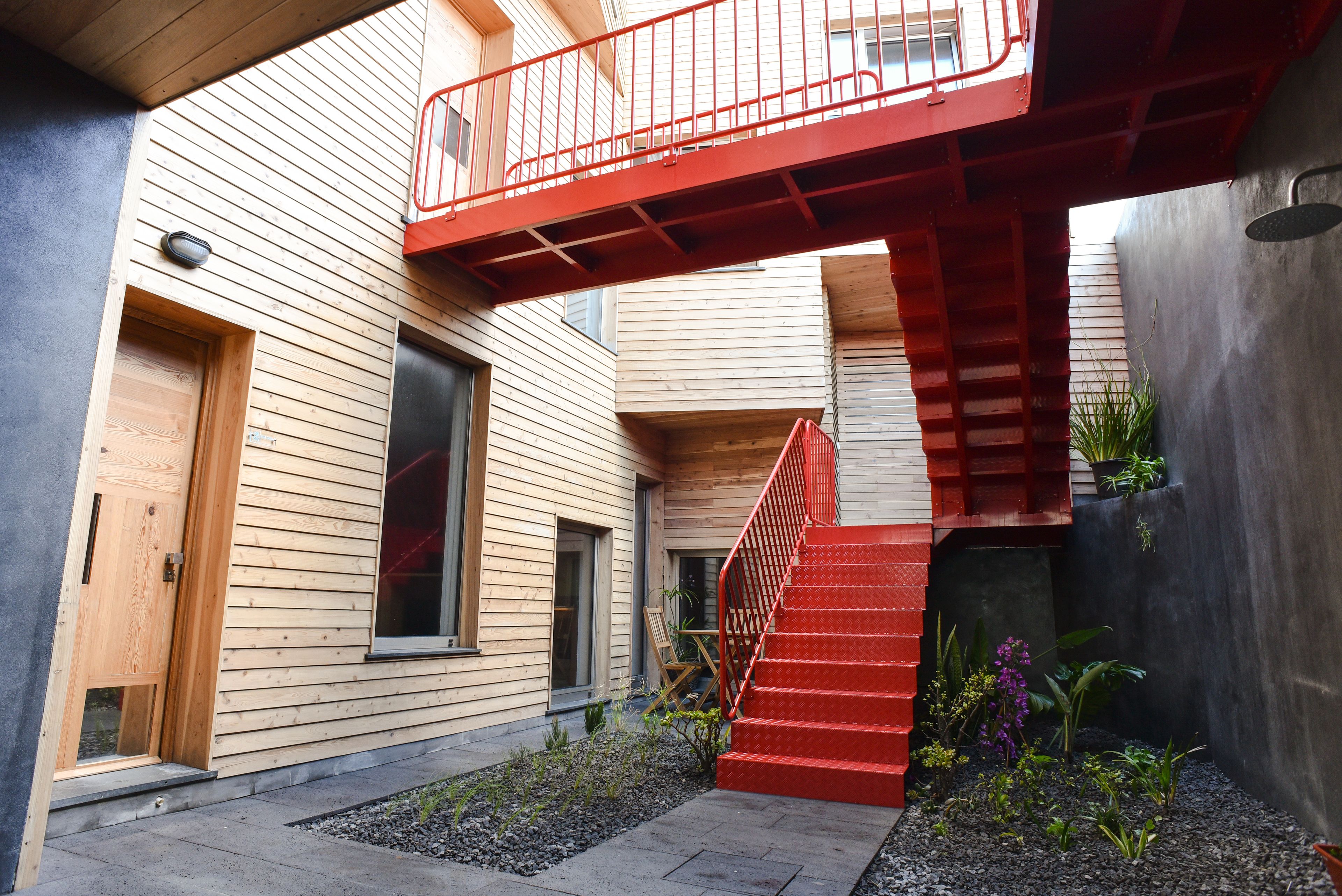 A modern building with a wooden exterior, a red staircase, and a small garden area.