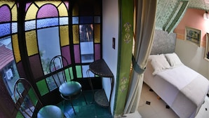 A room with a bed, a chair, a small table, and a view through a stained glass window. - Pousada Estalagem de Brotas (Brotas)