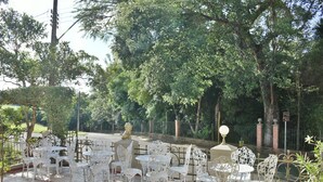 An outdoor seating area with white metal chairs and tables, surrounded by trees and a brick wall. - Pousada Estalagem de Brotas (Brotas)