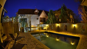 A swimming pool with a stone-tiled deck, lounge chairs, and a house in the background. - Pousada Estalagem de Brotas (Brotas)