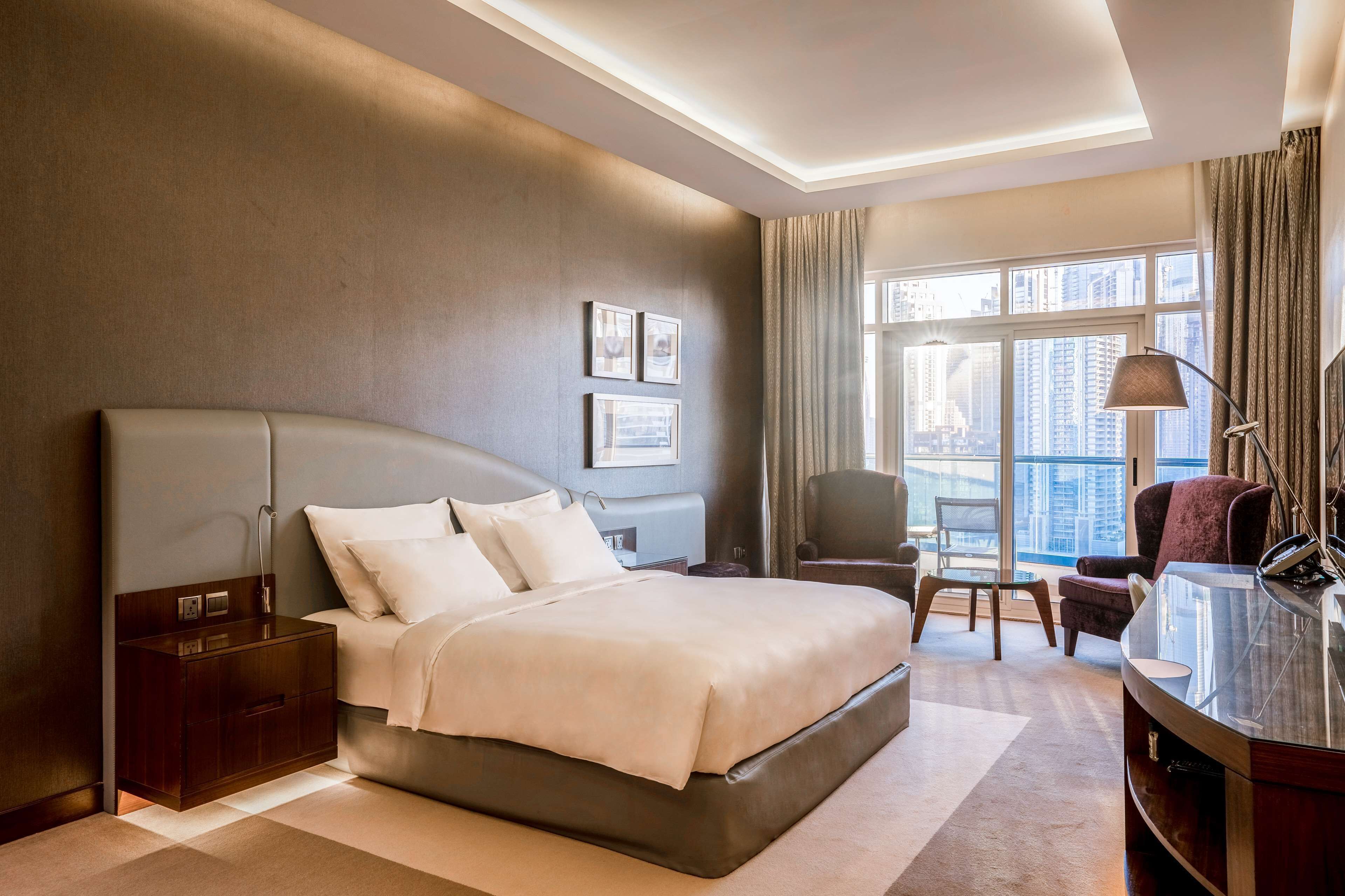 A modern hotel room with a large bed, a desk, and a view of the city.