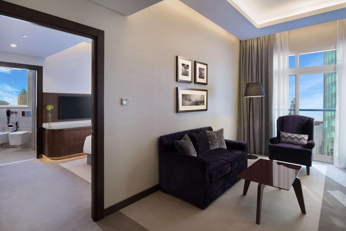 Ein modernes Hotelzimmer mit einer dunkelgrauen Couch, einem kleinen Holztisch und einem großen Fenster mit Blick auf die Stadt.