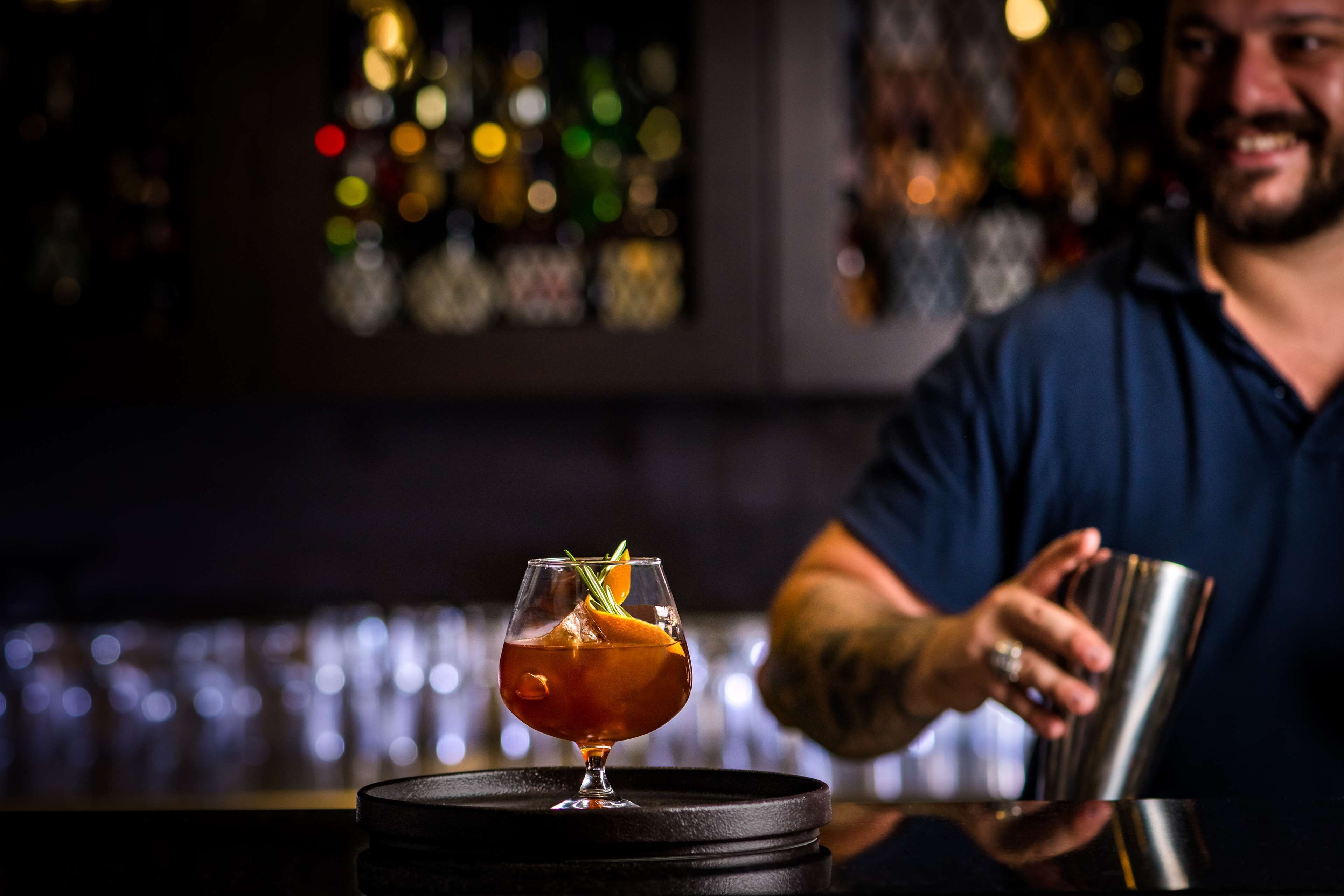 Ein Cocktail auf einer Bar, verschwommene Bar im Hintergrund mit Lichtern.