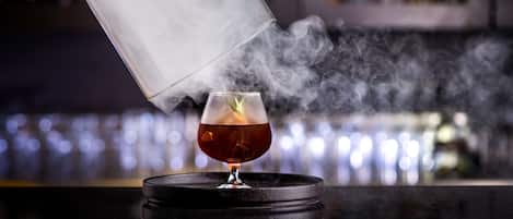 Une personne verse un liquide transparent dans un verre rempli de glaçons, ce qui crée une légère brume.