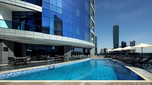 Ein modernes Hotel mit Pool auf dem Dach, Liegestühlen und Blick auf die Stadtlandschaft.