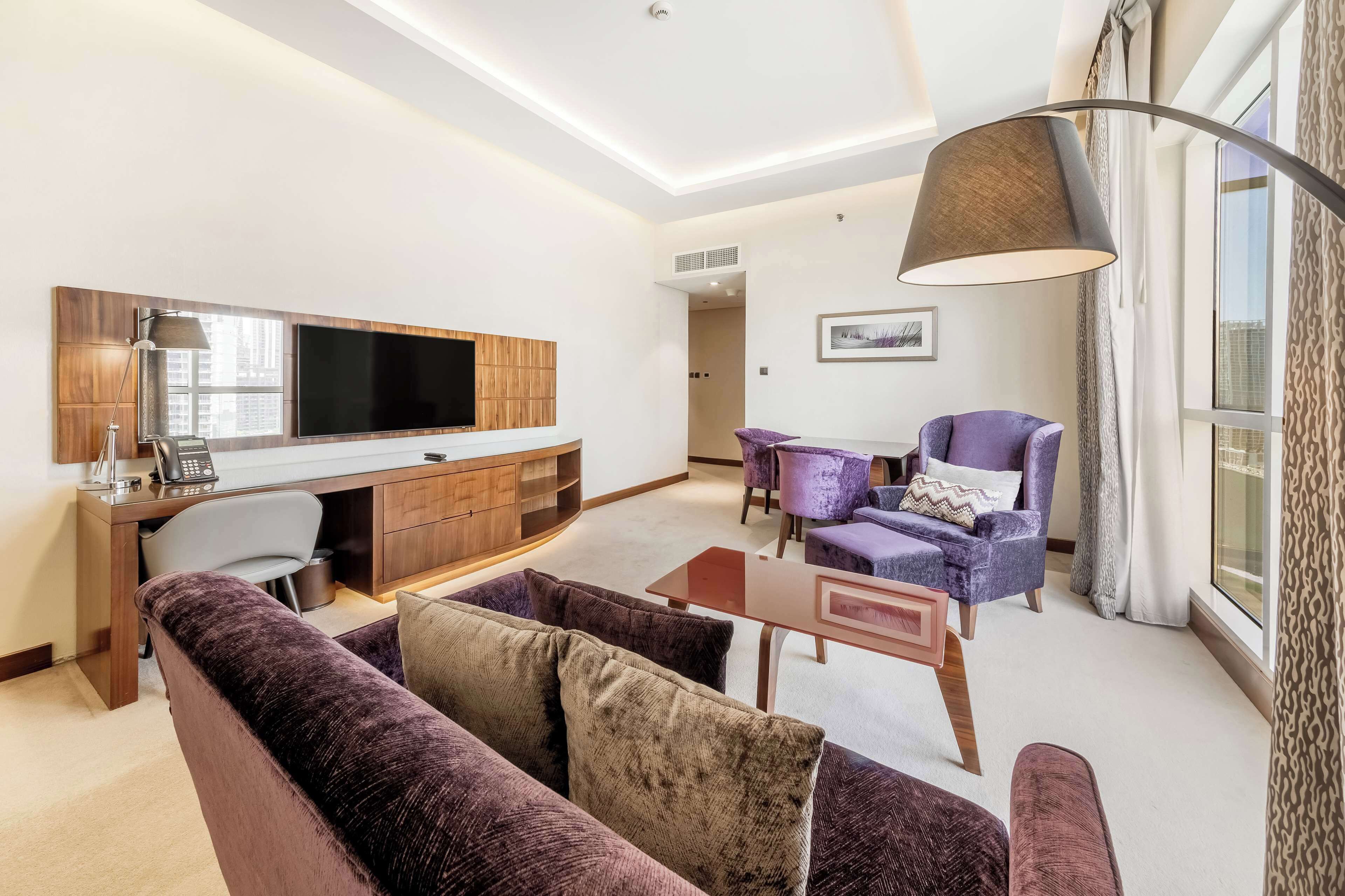 A modern living room with a sofa, a desk, a TV, and a lamp.