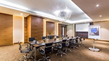 A conference room with a long table, multiple chairs, a projector screen, and a large chandelier.