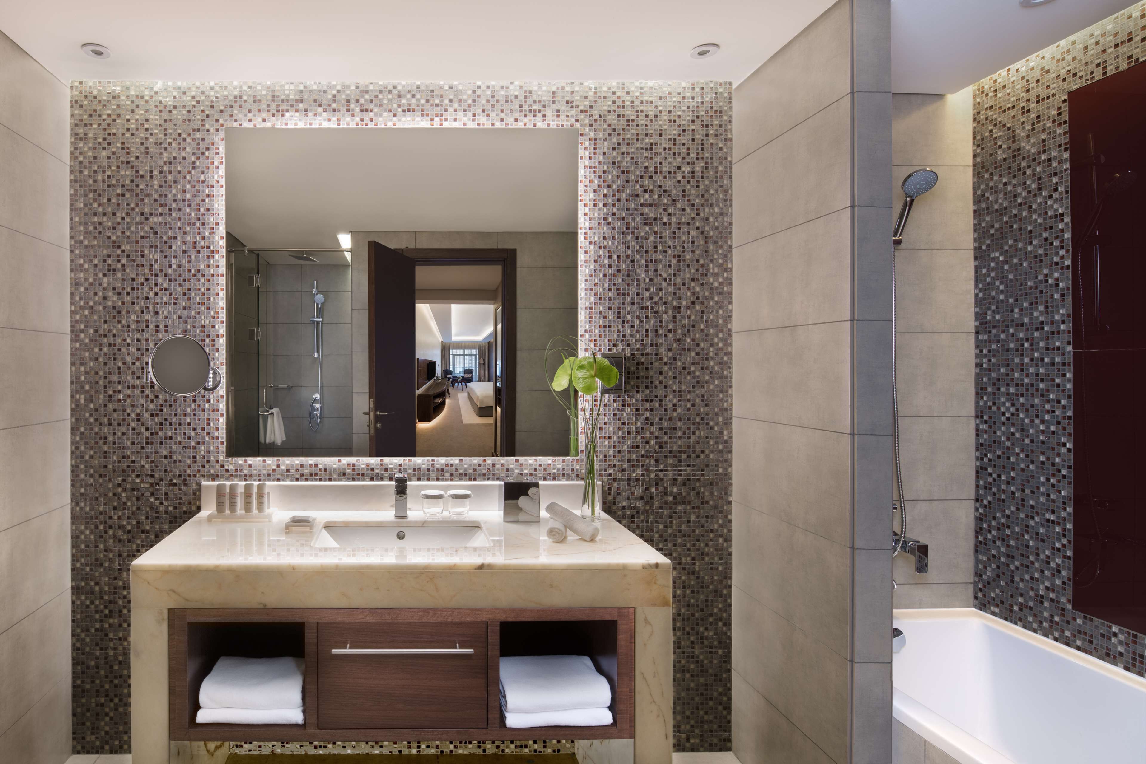 A modern bathroom with a large mirror, a sink, a shower, and a plant.