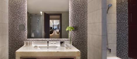 Un baño moderno con un espejo grande, un lavabo, una ducha y una planta.
