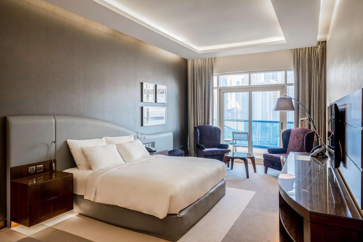 Ein modernes Hotelzimmer mit einem großen Bett, einem Schreibtisch, einem Sessel und einem Fernseher.