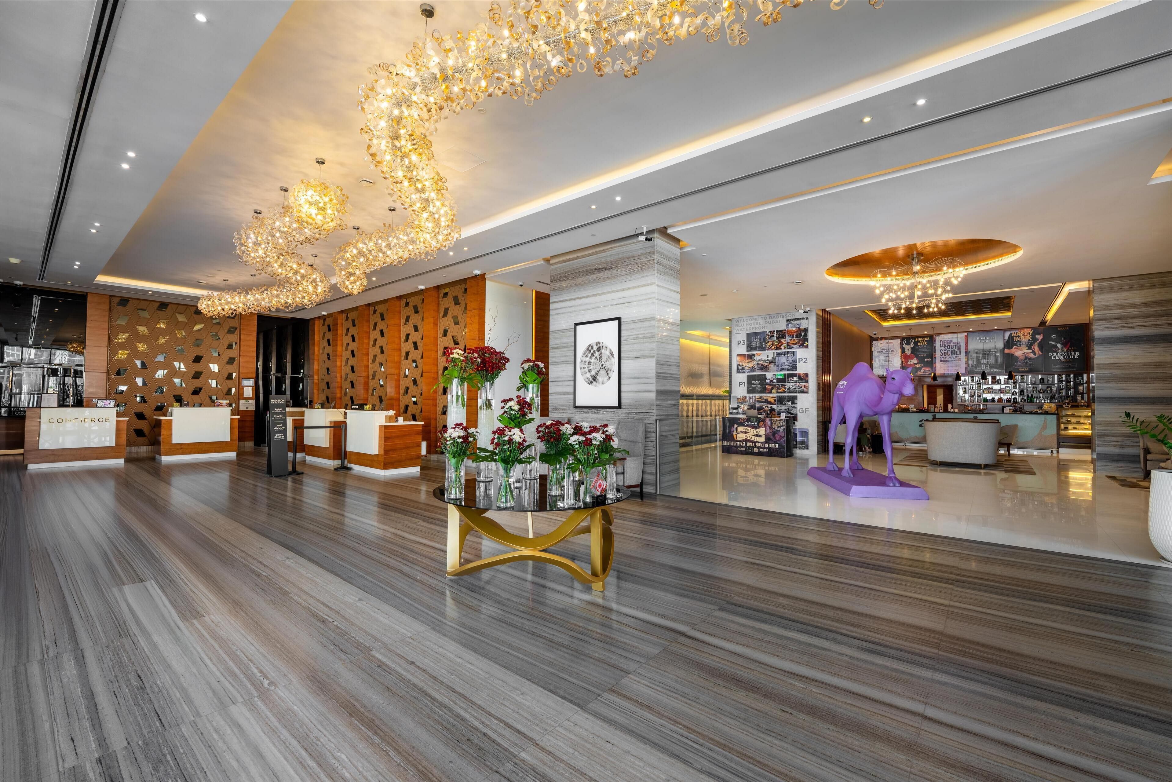 Un moderno vestíbulo de hotel con una recepción, una mesa decorativa con jarrones y una zona de bar.
