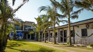 A building with a covered outdoor seating area, palm trees, and a clear sky. - Pousada Aventura (Passo de Torres)