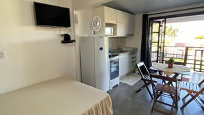 A bedroom with a bed, a TV mounted on the wall, a kitchenette with a microwave, and a dining area with a table and chairs. - Pousada Aventura (Passo de Torres)