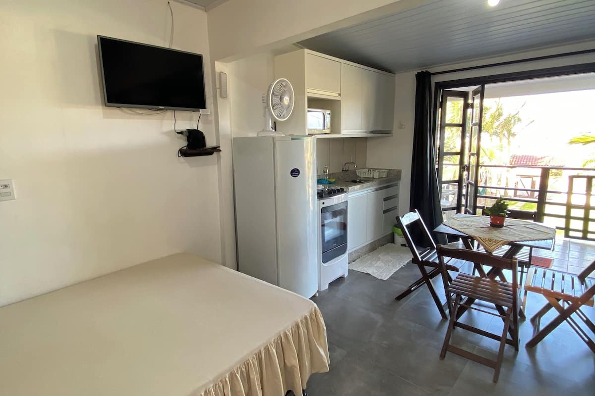 Ein Schlafzimmer mit einem Bett, einem an der Wand befestigten Fernseher, einer Küchenzeile mit einer Mikrowelle und einem Essbereich mit Tisch und Stühlen.