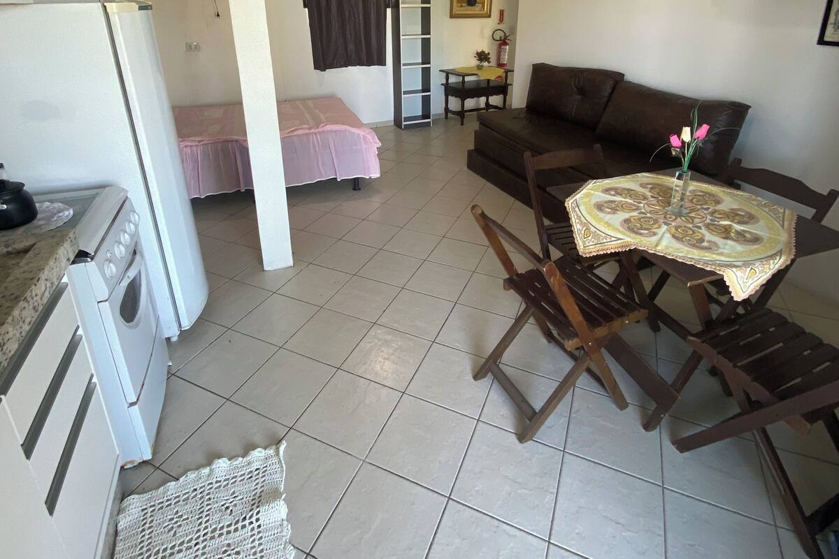 Ein kompakter Wohnbereich mit Küchenzeile, einer Essecke mit Tisch und Stühlen, einem Sofa, einem Bett und einem kleinen Tisch mit einer Vase.