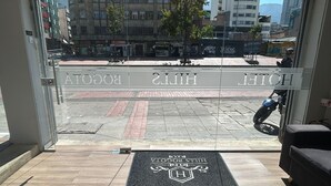 A hotel entrance with a clear view of the street outside, a doormat with the hotel's name, and a motorcycle parked outside.