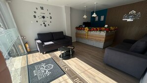 A hotel lobby with a sofa, a reception desk, a wall clock, and a wooden floor.