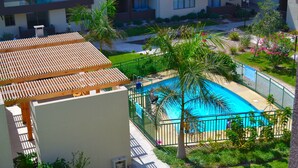 A rooftop pool area with a wooden pergola, surrounded by greenery and a fenced swimming pool. - Apartamentos Alma Surire (Arica)
