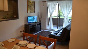 A dining area with a TV, a sofa, and a view to the outside. - Apartamentos Alma Surire (Arica)