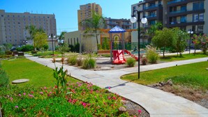 A playground with a slide and climbing structures, surrounded by well-maintained flower beds and a paved walkway. - Apartamentos Alma Surire (Arica)