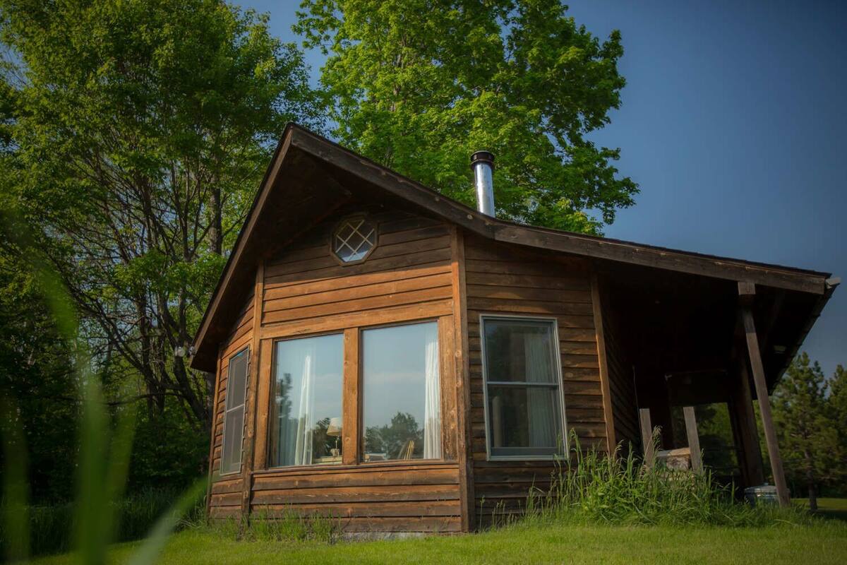 A wooden cabin with a pitched roof, large windows, and a chimney.