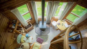 Een knus chalet met een centraal geplaatste open haard, houten wanden en grote ramen met uitzicht op de omgeving.