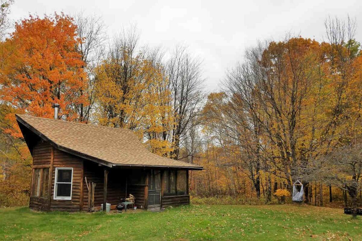 A rustic cabin with a sloped roof, a porch, and a small attached shed.