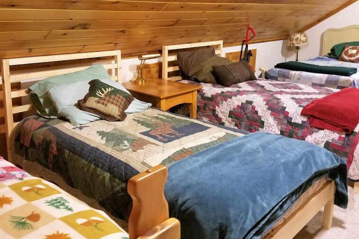 A cozy attic bedroom with wooden beams, three wooden beds, and a quilted bedspread.
