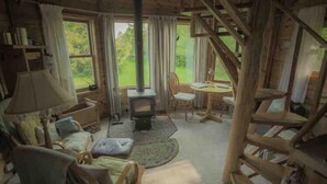 Een gezellig blokhutinterieur met een open haard, houten meubels en grote ramen met uitzicht op de natuur.