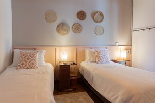 Habitación de hotel con dos camas, mesitas de noche con lámparas y decoración de pared tejida.