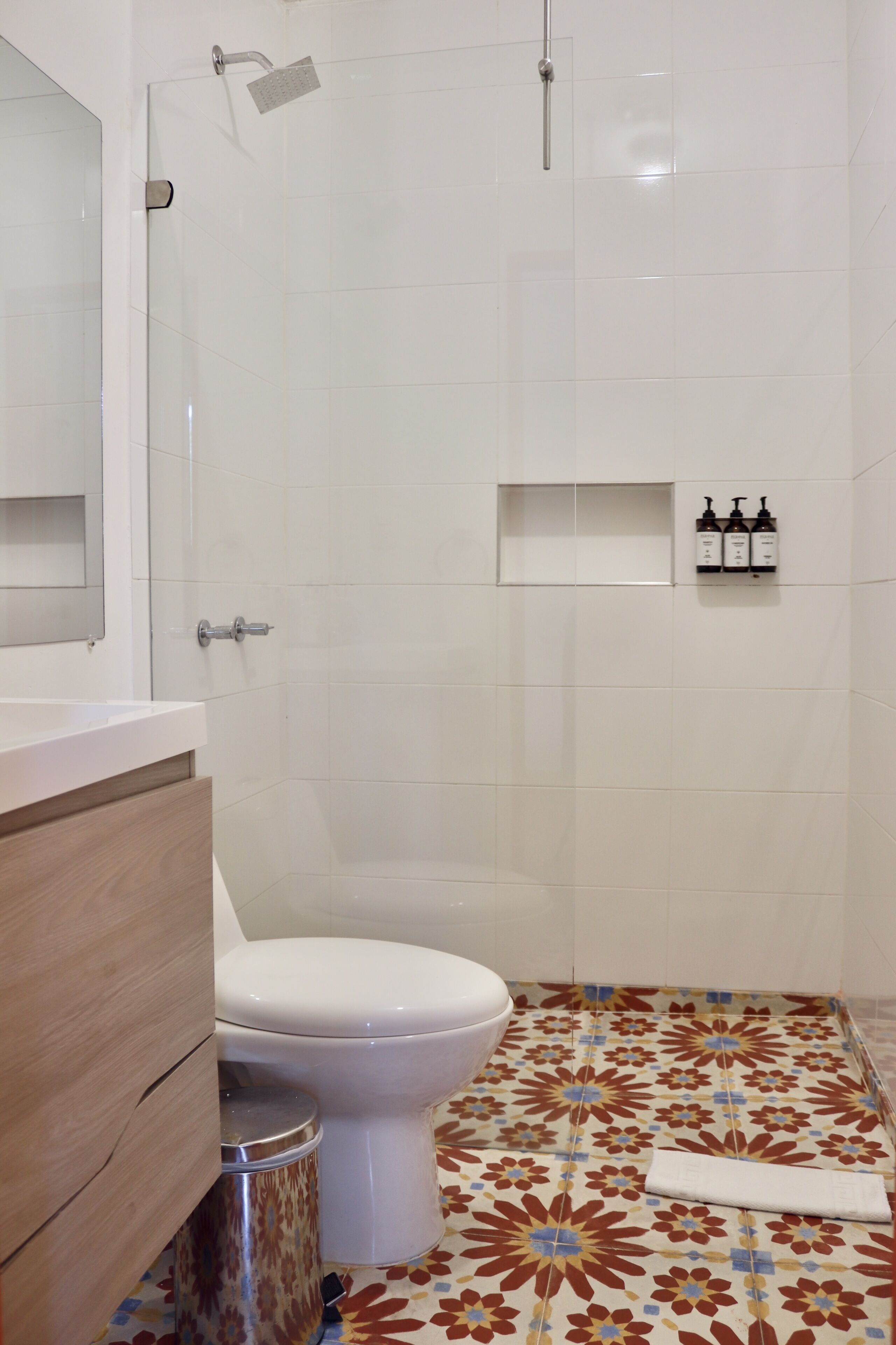 A bathroom with a toilet, a sink, a mirror, a shower, and a patterned floor.