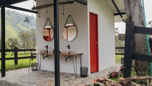 Un edificio pequeño con una puerta roja, dos lavamanos y dos espejos.