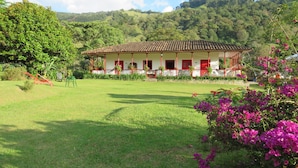 Un edificio con fachada roja y blanca, rodeado por un césped cuidado y plantas con flores.