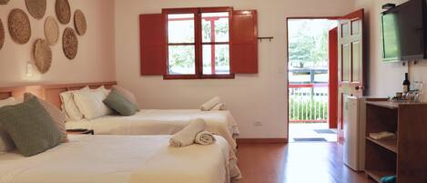 Habitación de hotel con dos camas, televisor, refrigerador y ventana con contraventanas rojas.