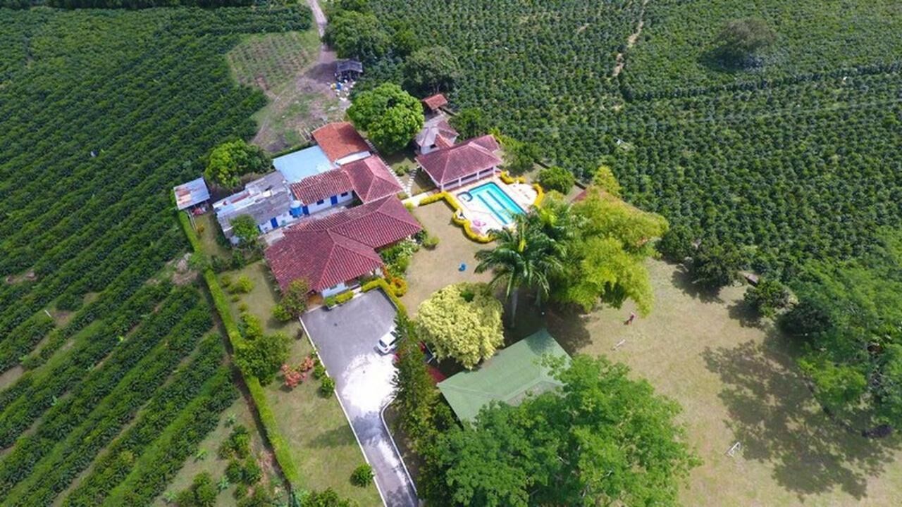 An aerial view of a property with a swimming pool, multiple buildings, and surrounding lush greenery.