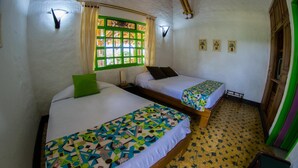 Een kamer met twee bedden, elk voorzien van een beddekleed met dessin, een raam met groene kaders en wandlampen.
