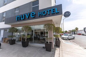 Un hotel llamado 'Nuve Hotel' con una fachada moderna, amplias ventanas y una zona de estar exterior con plantas en macetas.