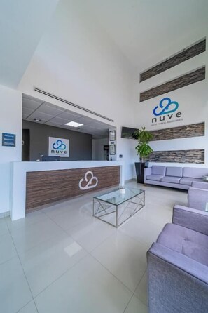 Un área de recepción moderna con mostrador, una mesa de centro de vidrio, zona de estar y un letrero con el logotipo 'nuve'.