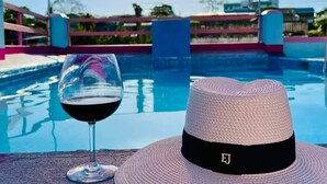 A poolside setting with a clear view of the pool, a glass of red wine, and a straw hat with the letter "EJ" on it. - Maya Bella Downtown Hotel (San Ignacio)