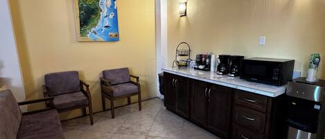 A kitchen with a microwave, coffee maker, and refrigerator. There are two chairs and a potted plant.