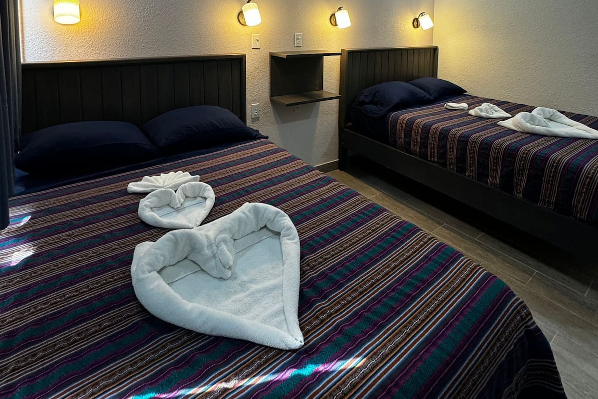 Quarto de hotel com duas camas, cada uma com cabeceira, ventilador de teto e luminárias fixadas na parede.