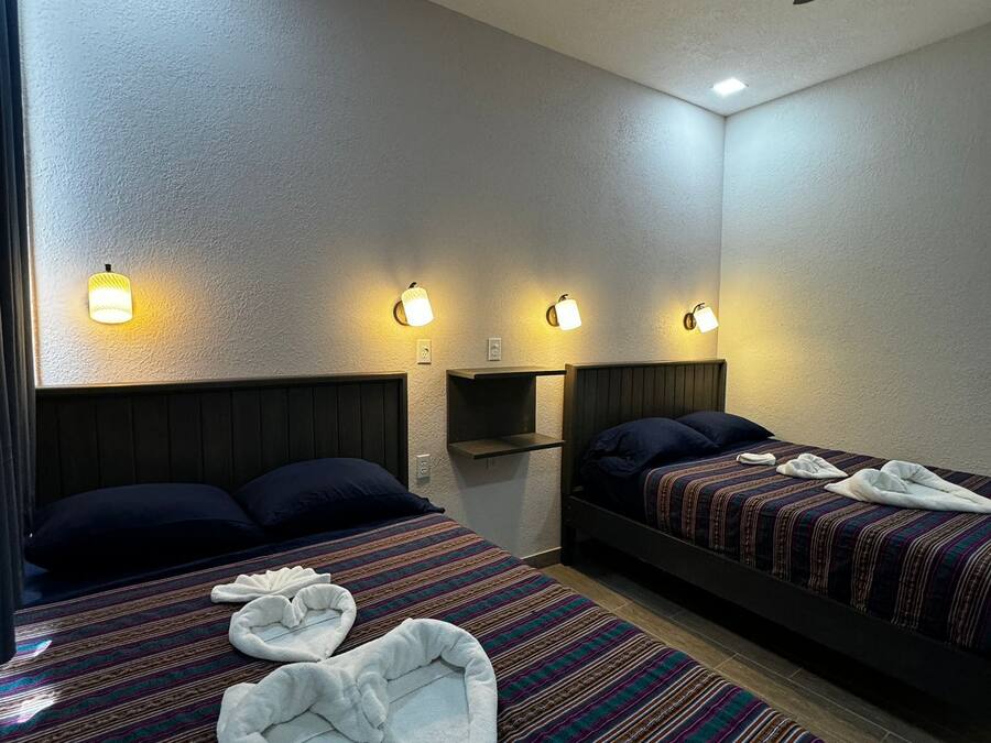 Hotellihuone, jossa on kaksi sänkyä, ja jokaisessa sängyssä on pääty sekä kattotuuletin ja seinään kiinnitetyt valaisimet.