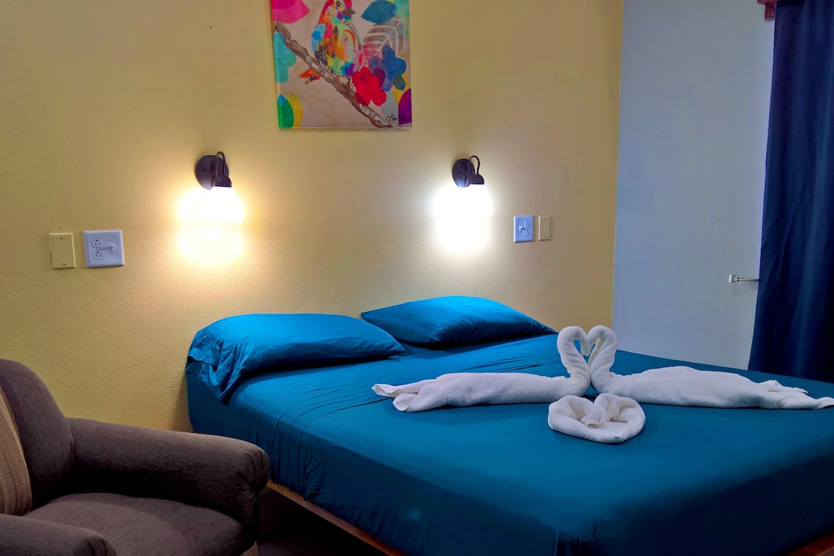 Quarto de hotel com uma cama, duas luzes fixadas na parede, um quadro e uma cortina azul.