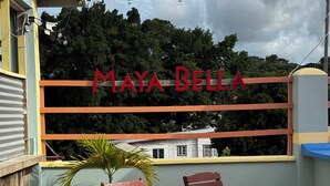 Ein Balkon mit zwei Holzstühlen, einem Topfpflanzen und einem Schild mit der Aufschrift 'MAYA BELLA'.