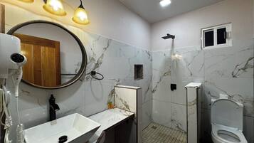 Um banheiro com pia branca, espelho, chuveiro manual e vaso sanitário.